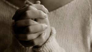 Mulher com as mãos juntas orando